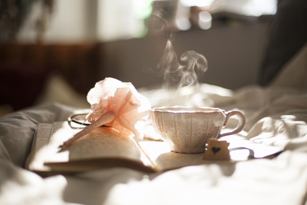 xícara de chá no livro ao lado da decoração da flor rosa