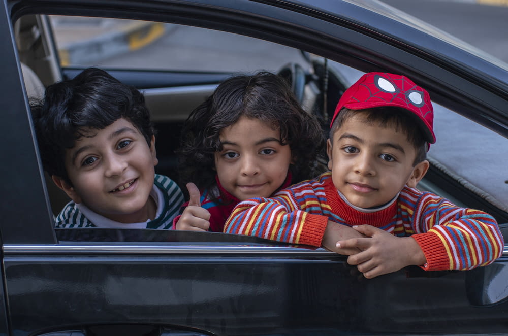 three boys looking outside window of car front seat