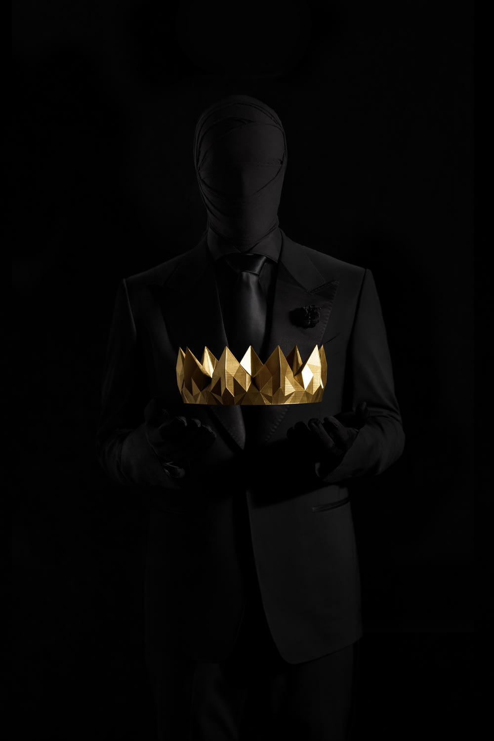 person in black suit jacket holding gold crown