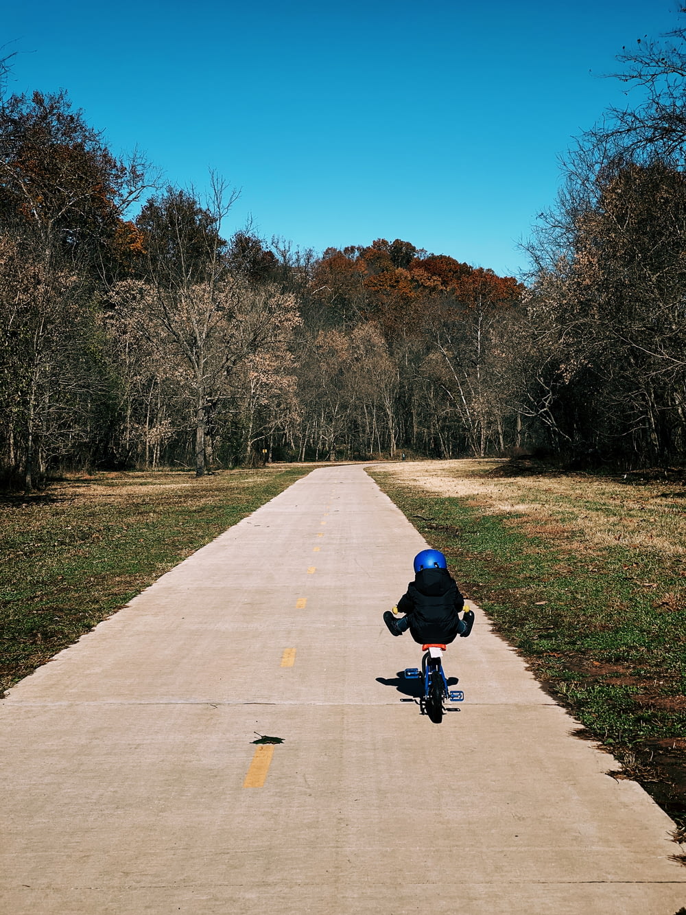 child biking on road near green field during daytime