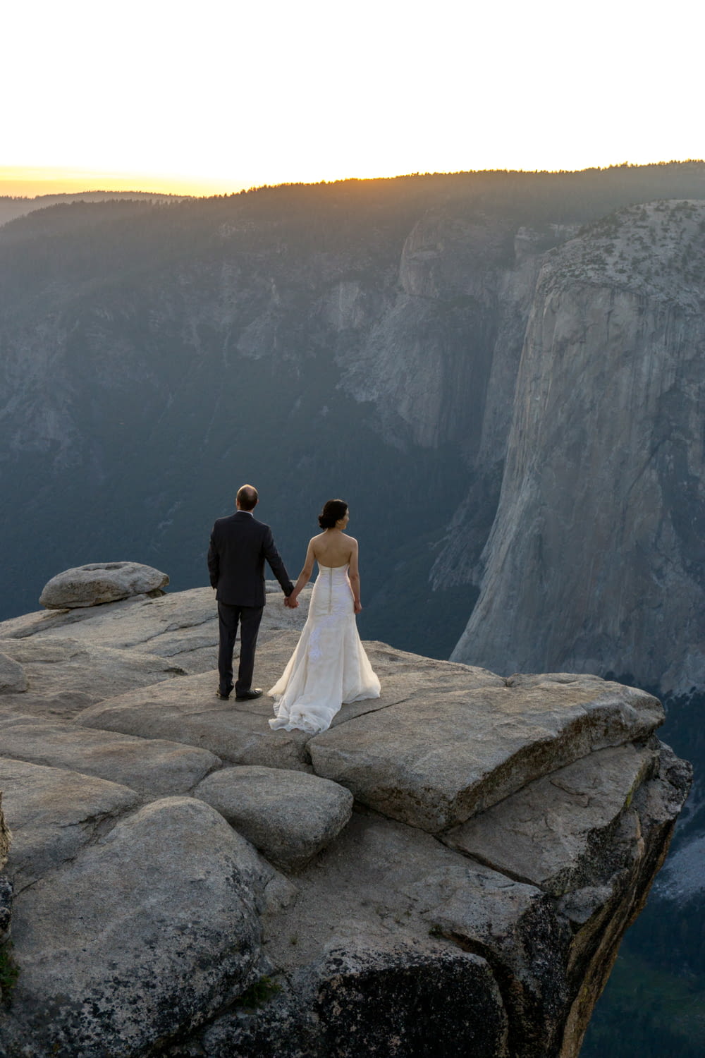bride and groom standing on rocky hill viewing Yosemite National Park during daytime