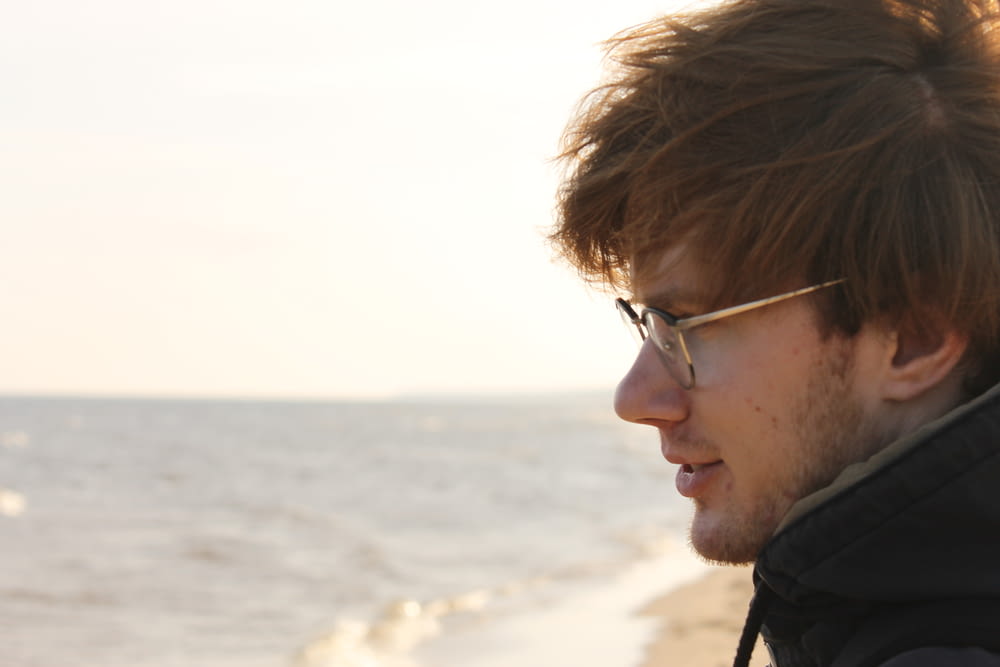 a man with glasses looking at the ocean