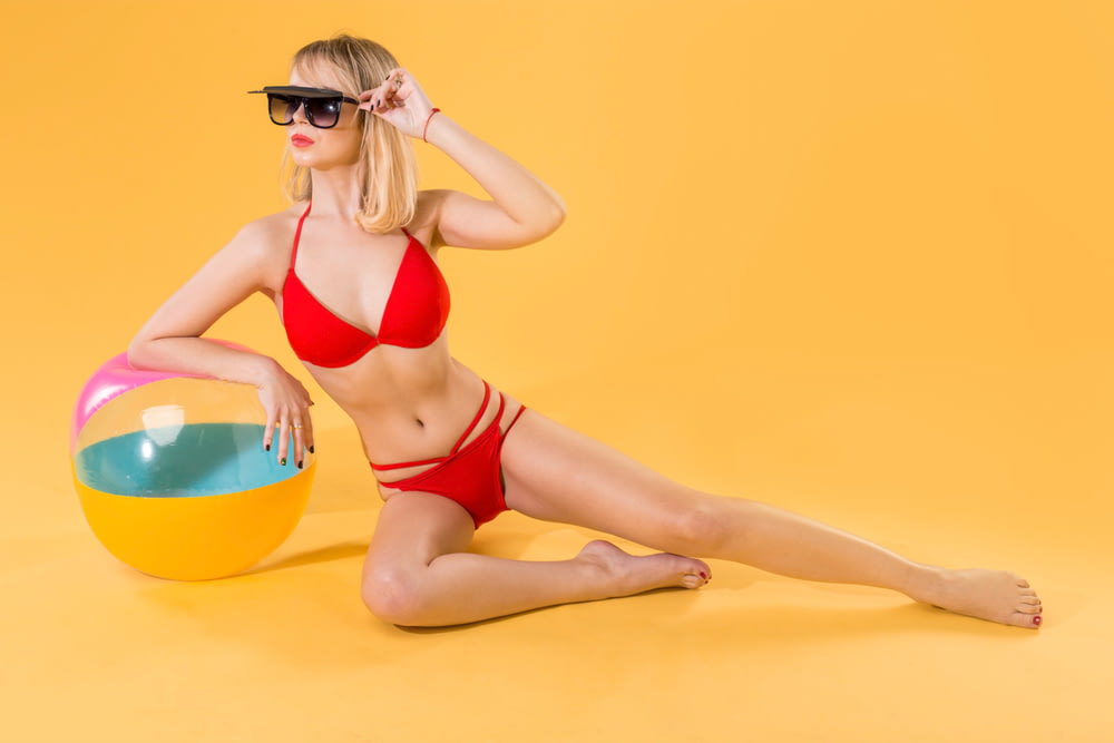 woman wearing red bikini sitting sideways on beach ball