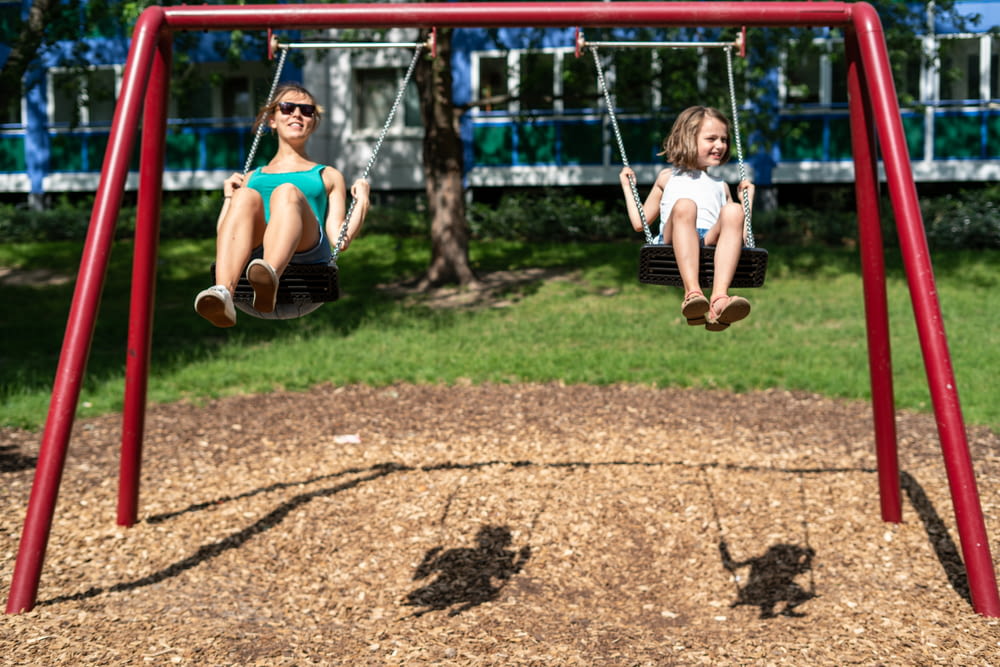 girl in blue shirt and brown shorts sitting on swing during daytime