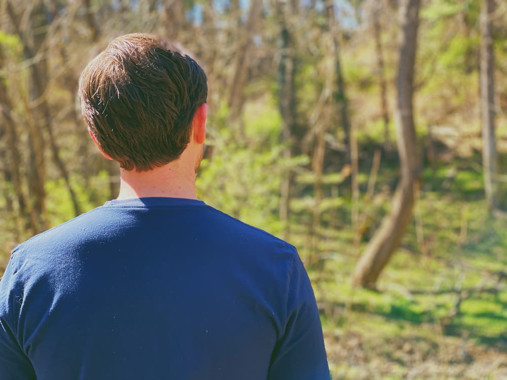 Mann im blauen Rundhalshemd tagsüber im Wald stehend