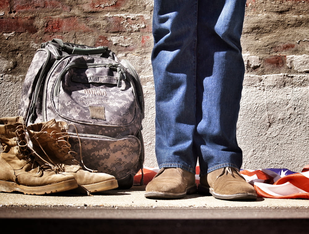 Fotografía minimalista de una persona de pie cerca de la mochila y las botas