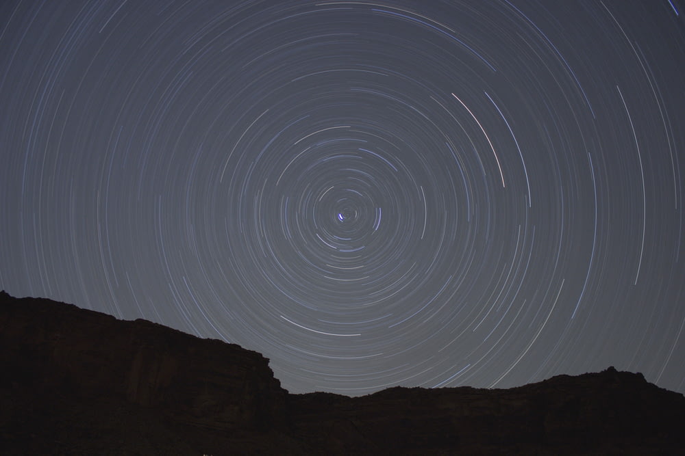 Cercles concentriques créés par des étoiles se déplaçant dans le ciel nocturne au-dessus d’une paroi rocheuse en silhouette