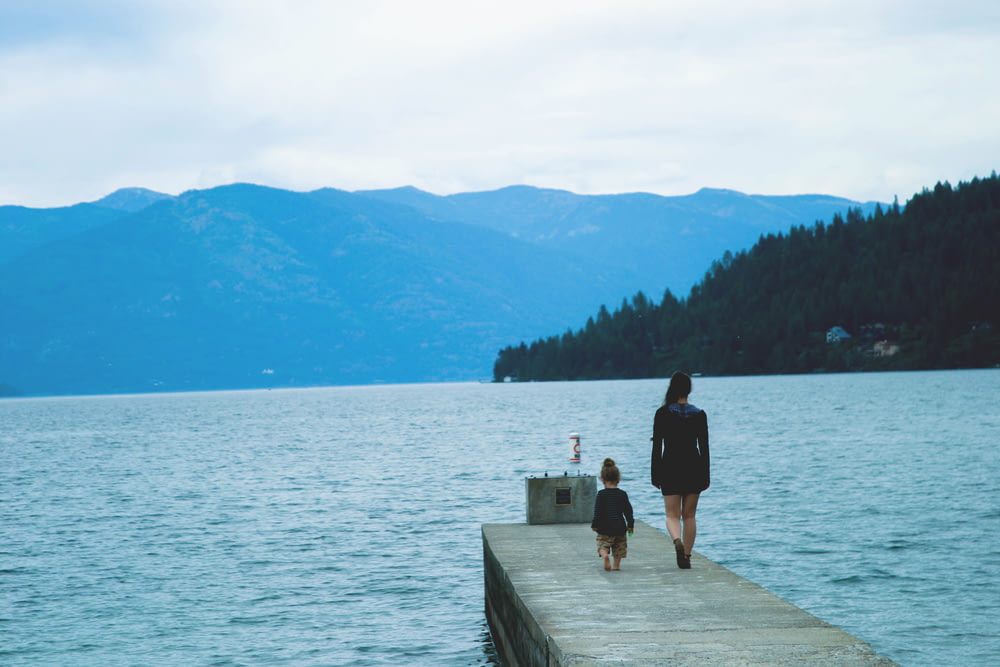 woman and girl walking along concrete dock surrounded by body of water