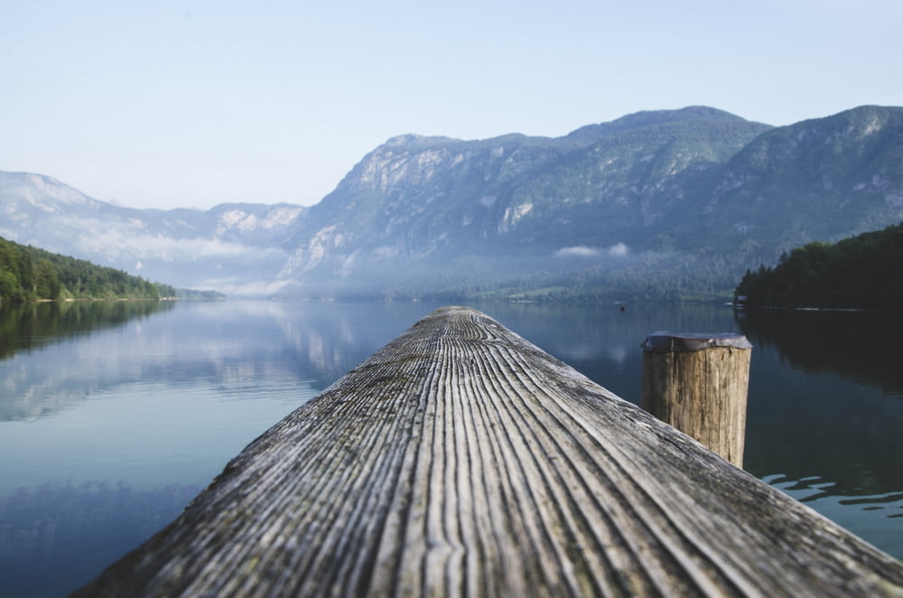 gray wood beam near body of water surrounded by mountain ranges during daytime