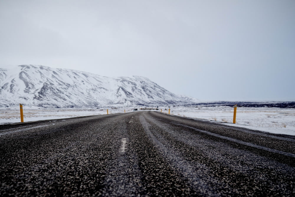 Carretera asfaltada cerca de la montaña llena de nieve bajo el cielo nublado
