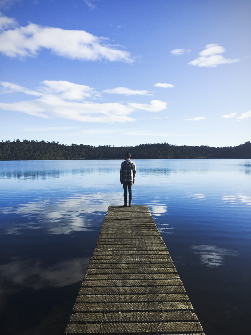 man standing on lake dock watching water under blue sky during daytime
