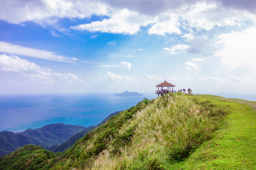 brown gazebo on top of green mountain overlooking sea during daytime landscape photography