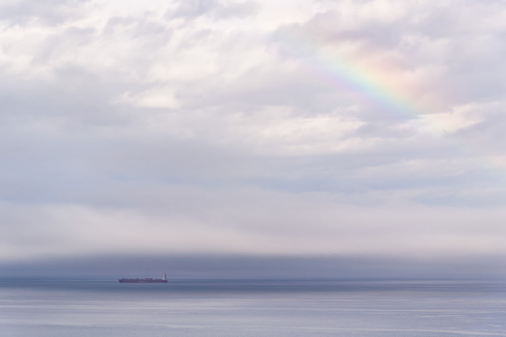 Schiff auf dem Ozean unter bewölktem Himmel mit Regenbogen