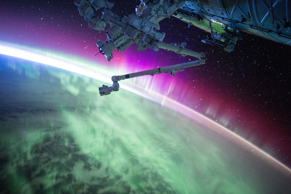 회색 공간 위성 아래의 보라색과 녹색 오로라 빔 사진