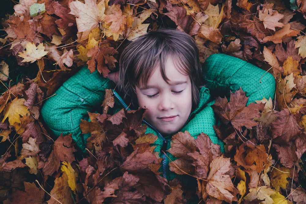茶色のカエデの葉の上に横たわっている閉じた目の男の子
