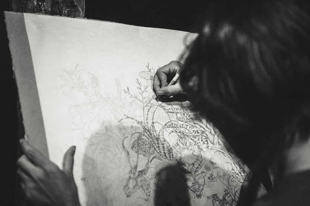 foto in scala di grigi di una donna che disegna un fiore