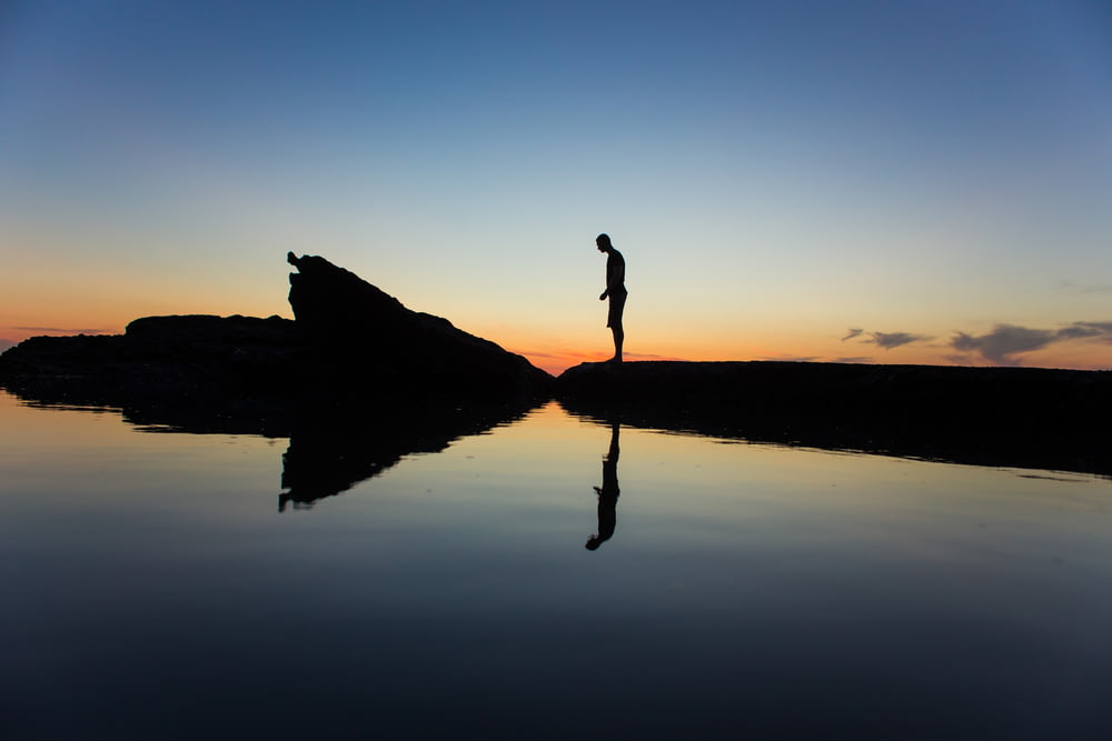 Silhouette eines Mannes, der auf dem Land in der Nähe eines Gewässers mit Reflexion steht