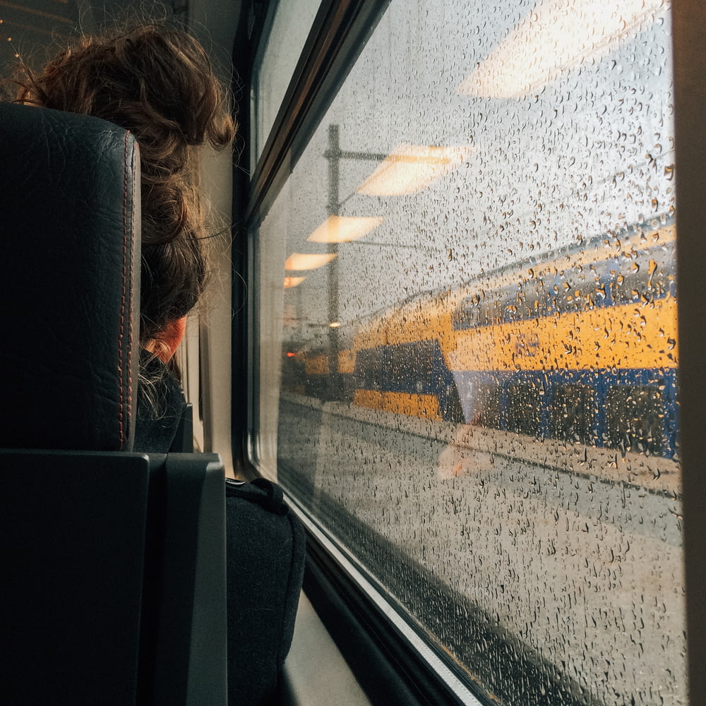 a woman looking out a train window on a rainy day