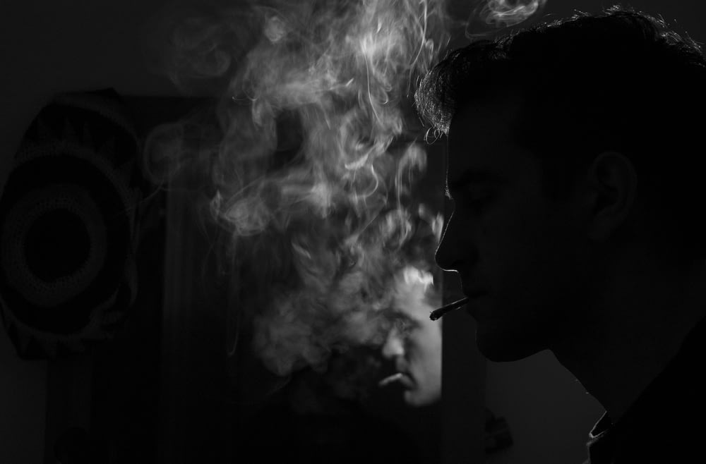 Fotografía en escala de grises de un hombre fumando un cigarrillo