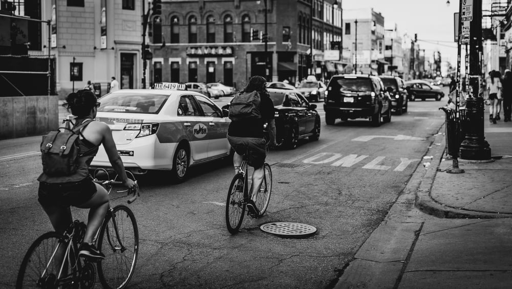 grayscale photo of two person riding bicycle on road
