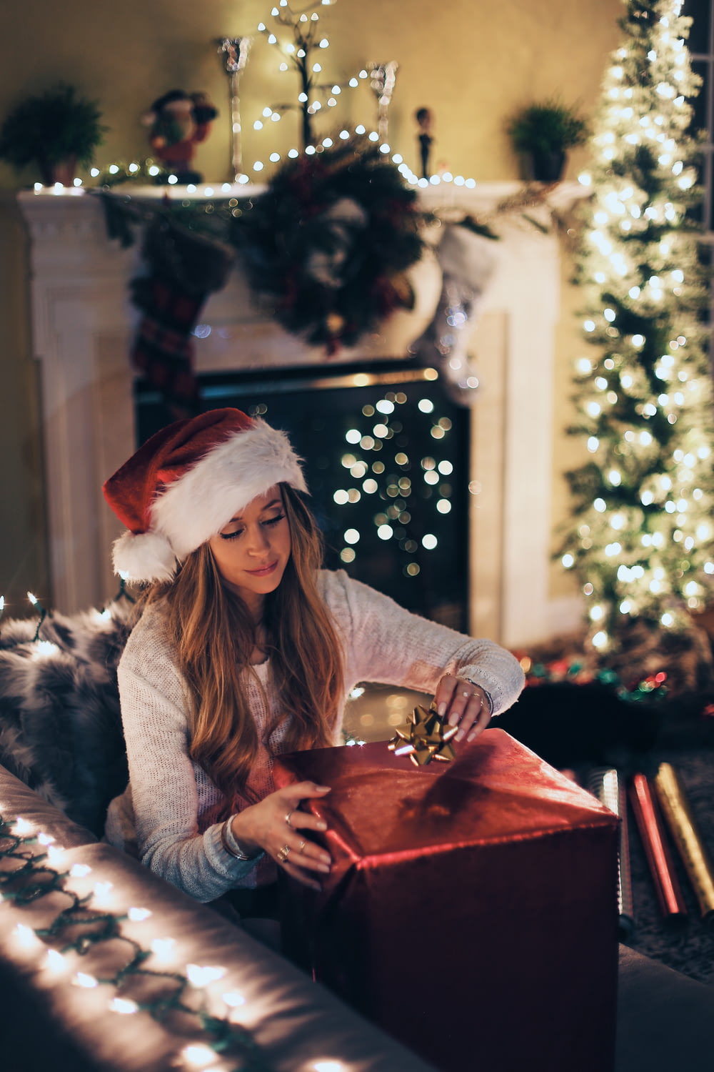 Frau legt Band in rote Geschenkbox in der Nähe des beleuchteten Weihnachtsbaums im Zimmer