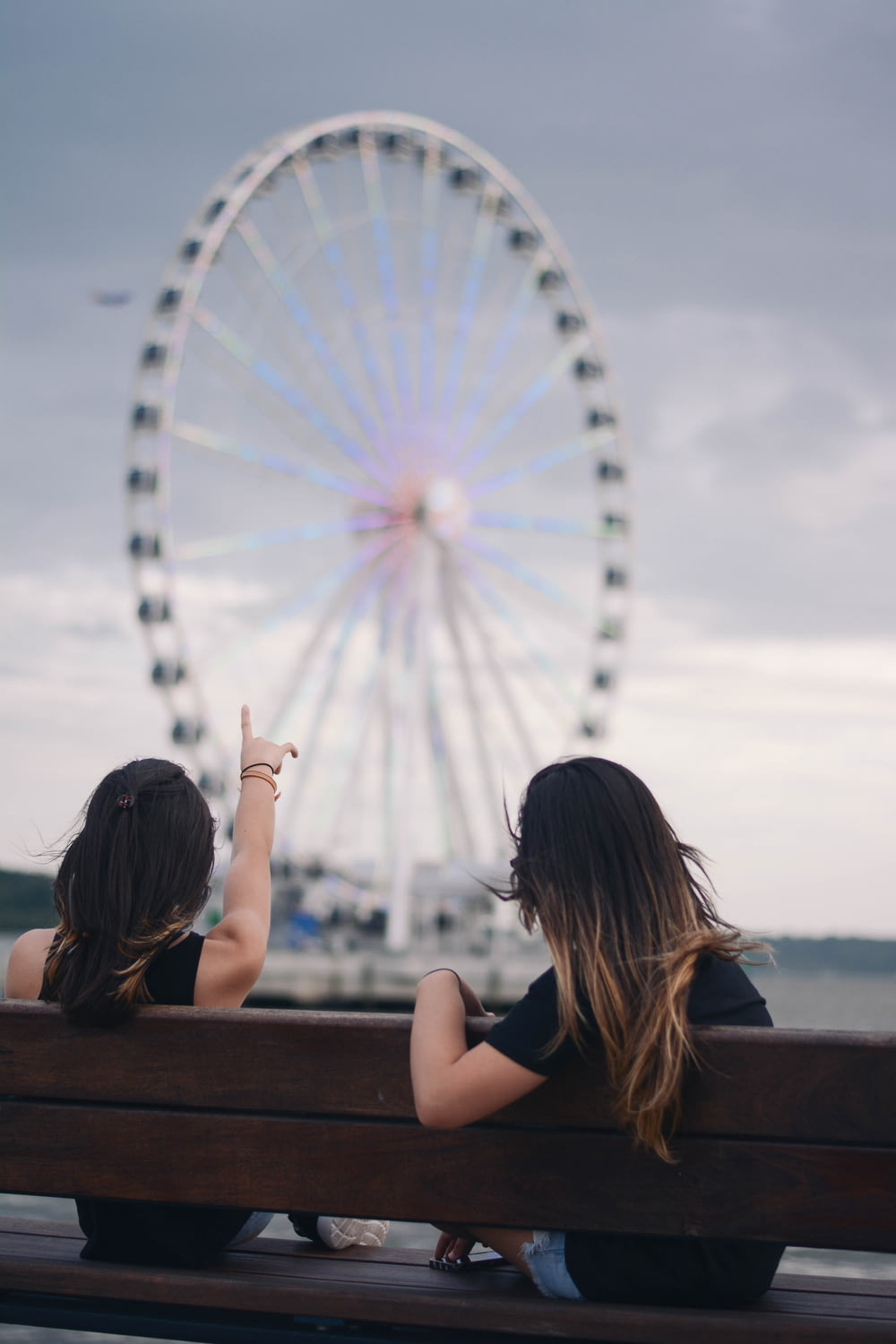 two women sitting on bench pointing white and blue Ferris wheel