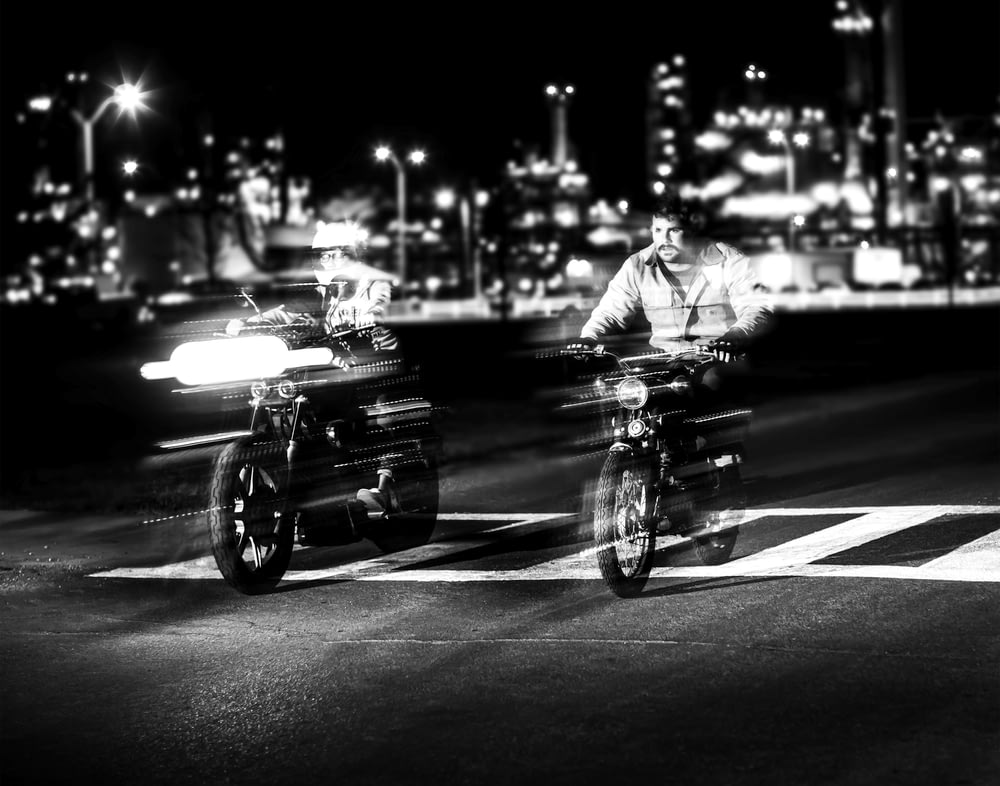 grayscale photo of person riding motorcycle near building and street lights