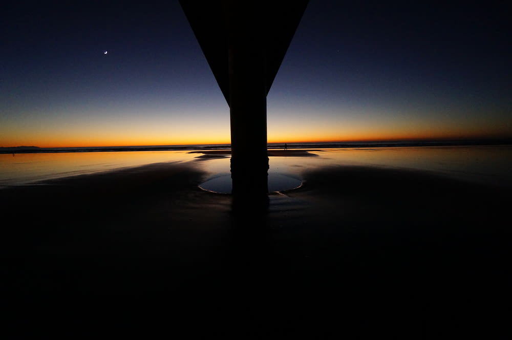 The sun-kissed horizon looms behind the pillar and across the water at dusk at New Brighton