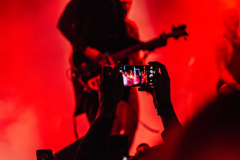 person holding smartphone in front of a person playing guitar on stage