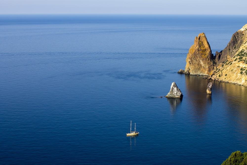 aerial photography of white ship on sea near rock formations under blue sky during daytime
