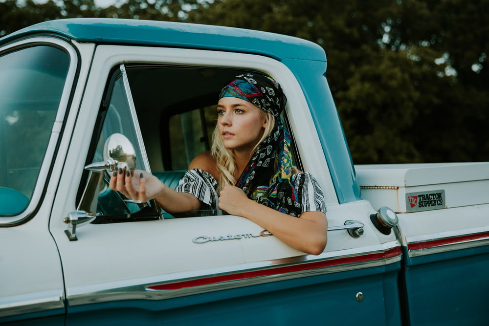 白と緑の2ドアピックアップトラックでサイドミラーを持つ女性の写真