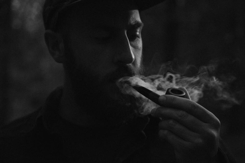 Photo en niveaux de gris d’un homme utilisant une pipe à fumer
