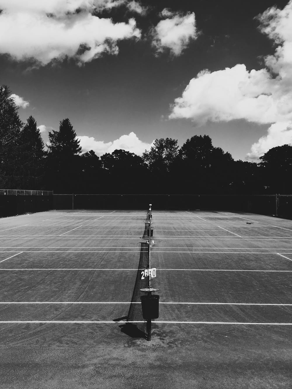 A look down the middle of a tennis net with a darkened background on a partially cloudy day.