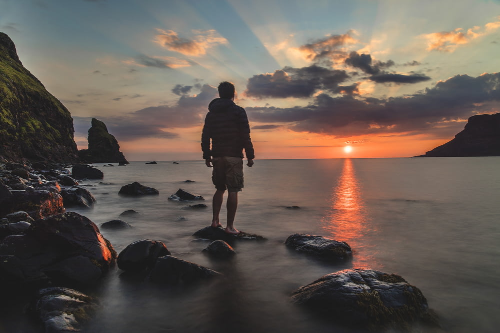 uomo in piedi sulla pietra che guarda il tramonto