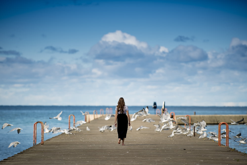 woman standing on a boardwalk surrounded by birds