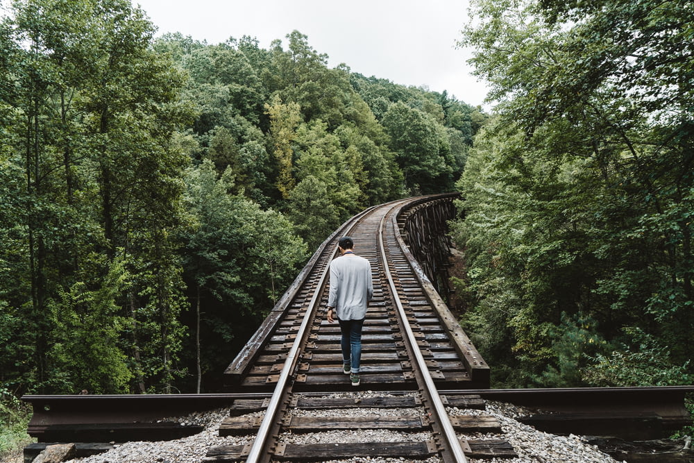 man standing on railway surrounded by trees