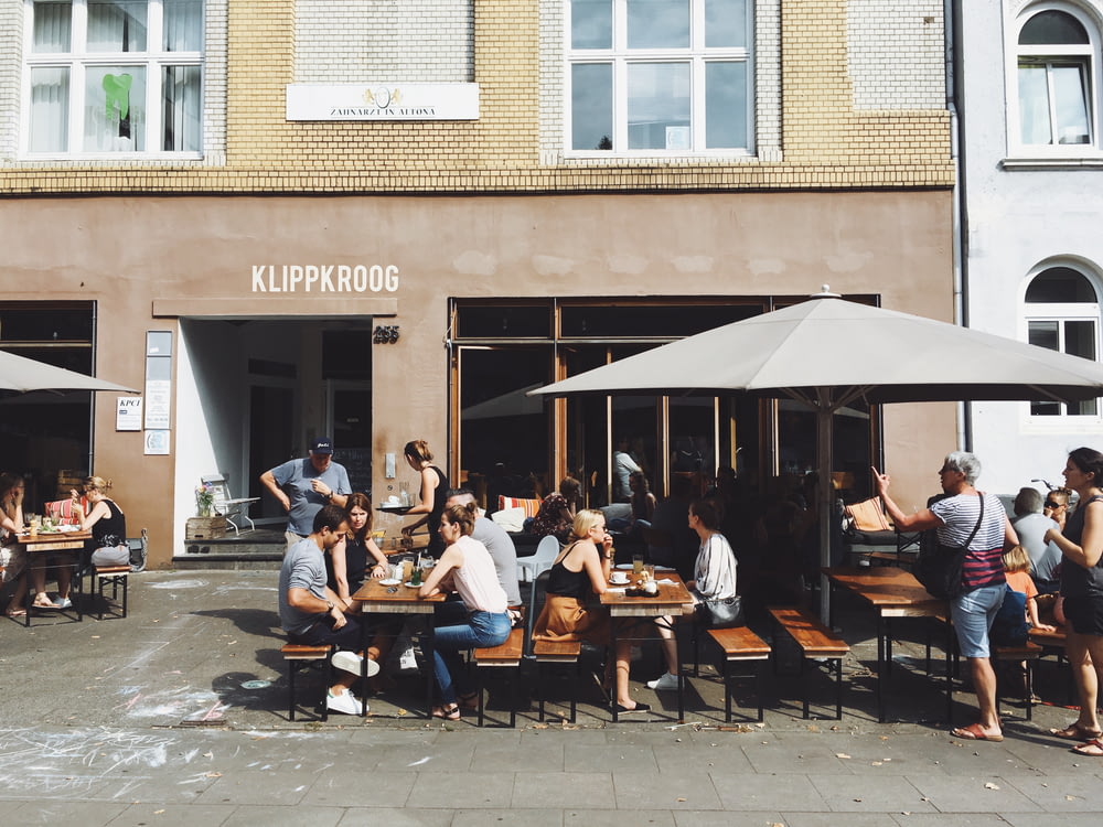 group of people sitting on benches with tables beside Klippkroog store front at daytime