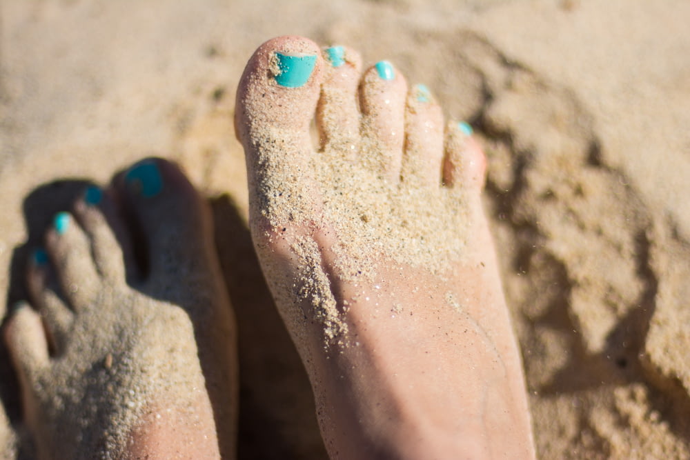 personne vernis à ongles bleu ciel pieds sur sable brun