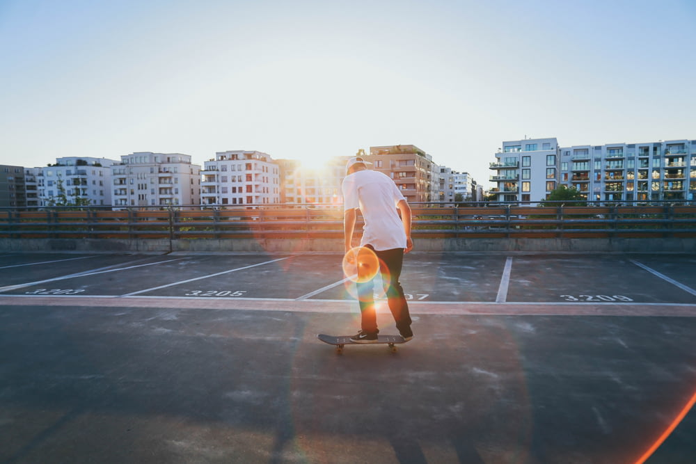man riding skateboard on parking lot near buildings during golden hour