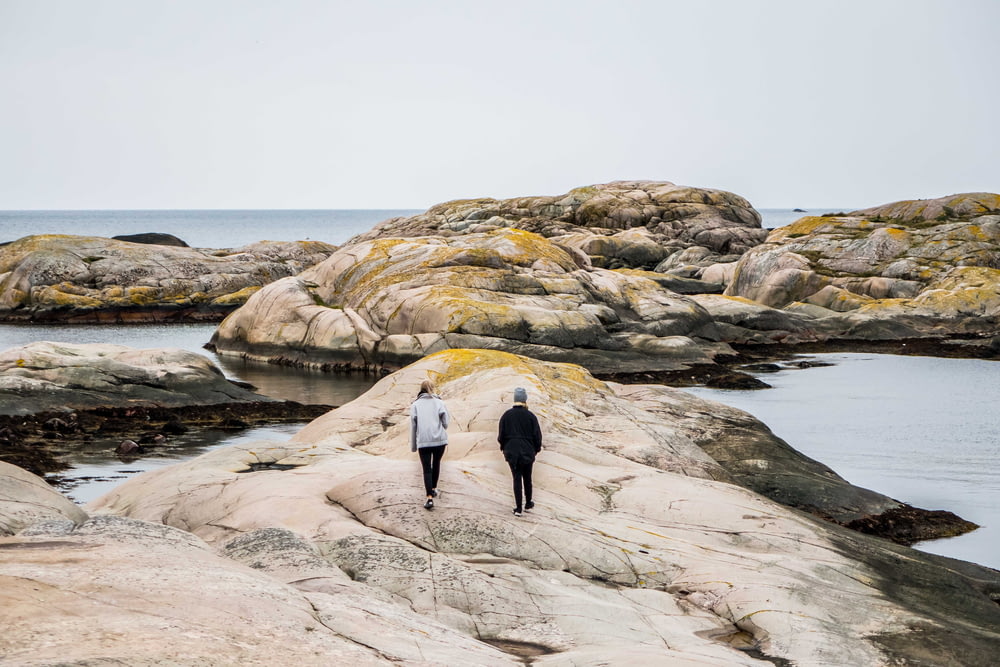 woman and man walking on rock formation near body of water during daytime