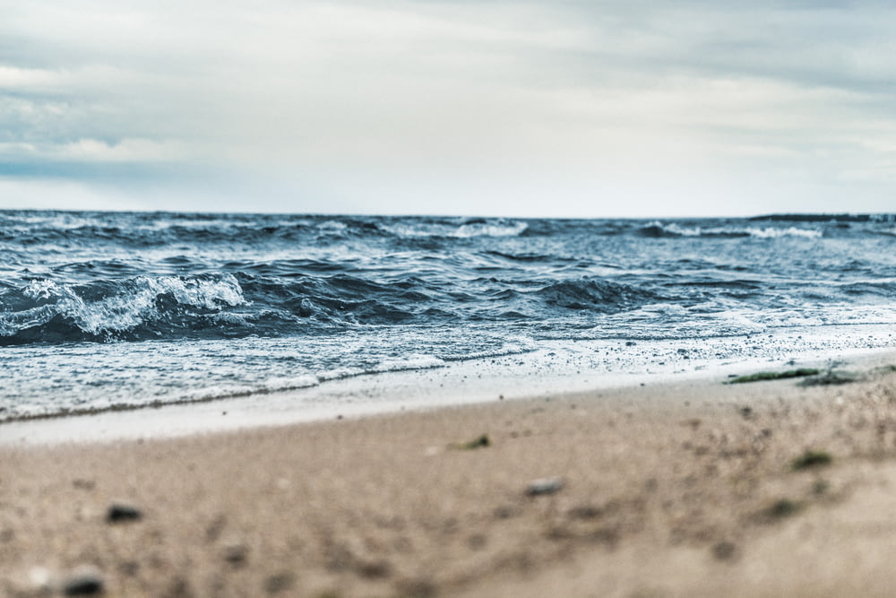 Fotografía de ángulo bajo de arena marrón al lado del cuerpo de agua bajo cielo blanco y azul durante el día