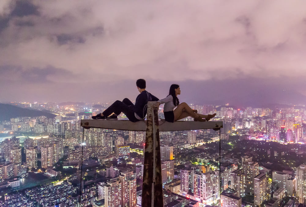 man and woman sitting on metal on top of high rise building