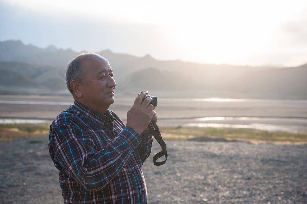 man holding camera standing with mountain background