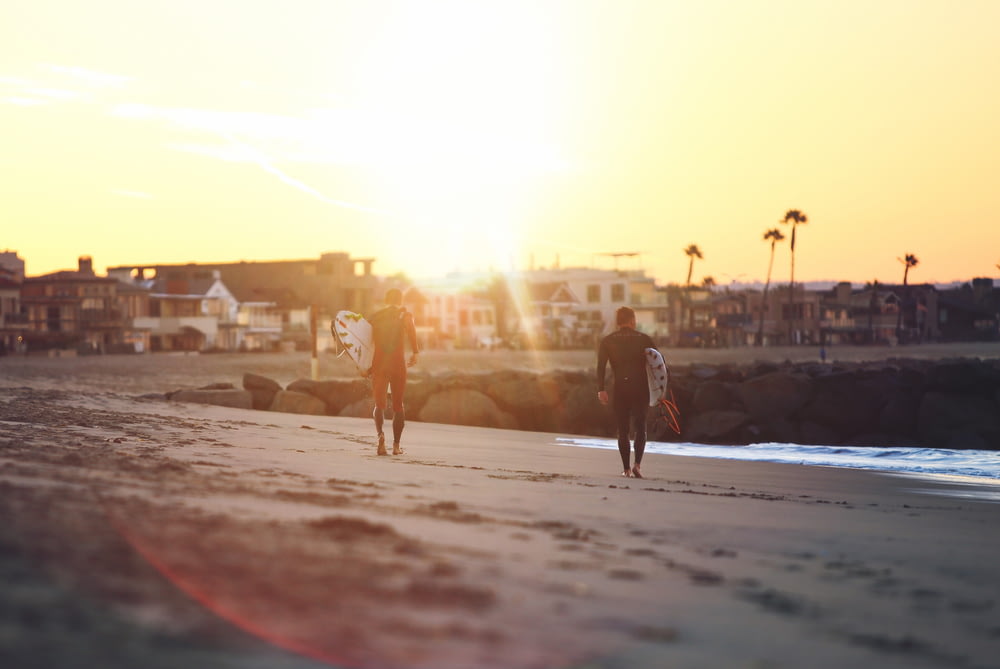 duas pessoas caminhando à beira-mar enquanto seguram pranchas de surfe