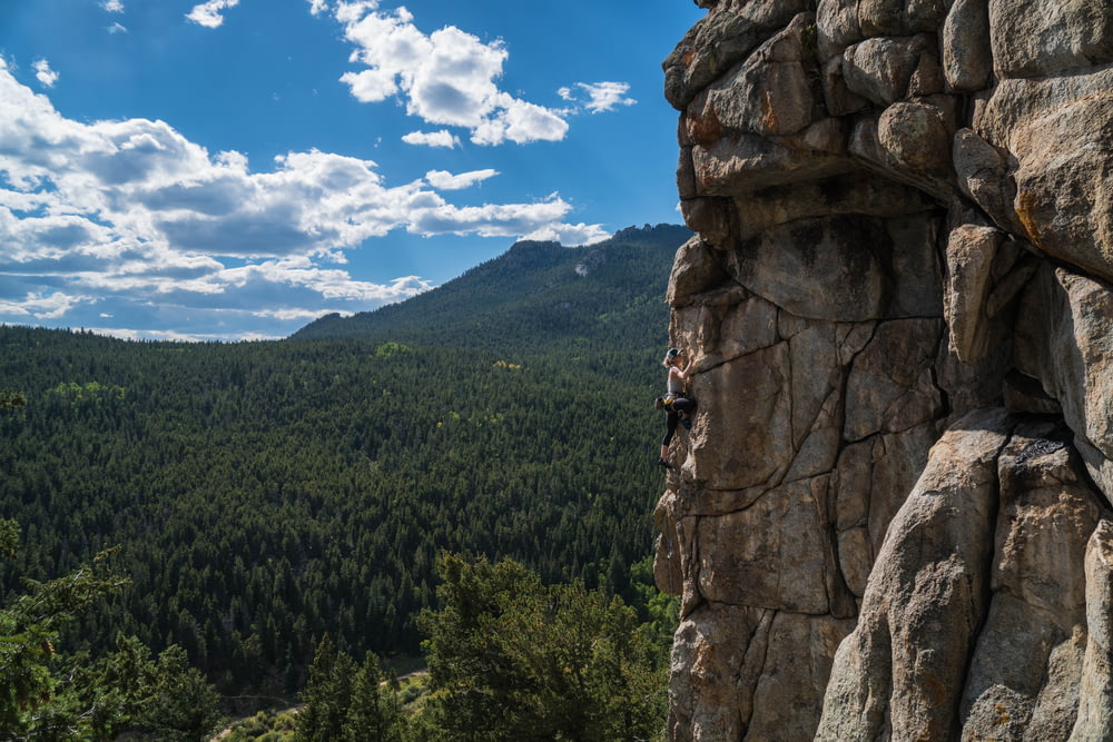 person doing rock climbing under white clouds at daytime