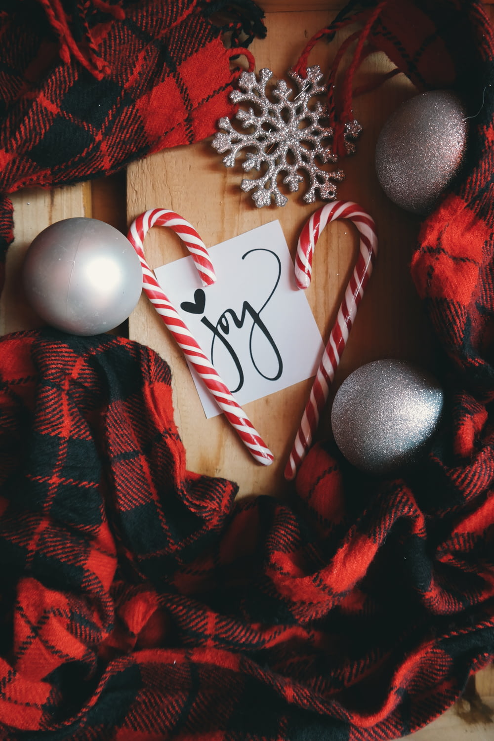 A white note that says "Joy," surrounded by candy canes, XMAS ornaments and red plaid material.