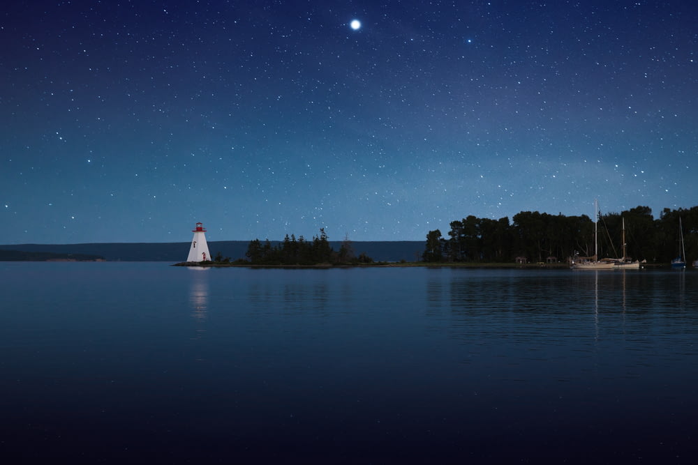 Photographie d’un phare blanc près d’un plan d’eau calme la nuit