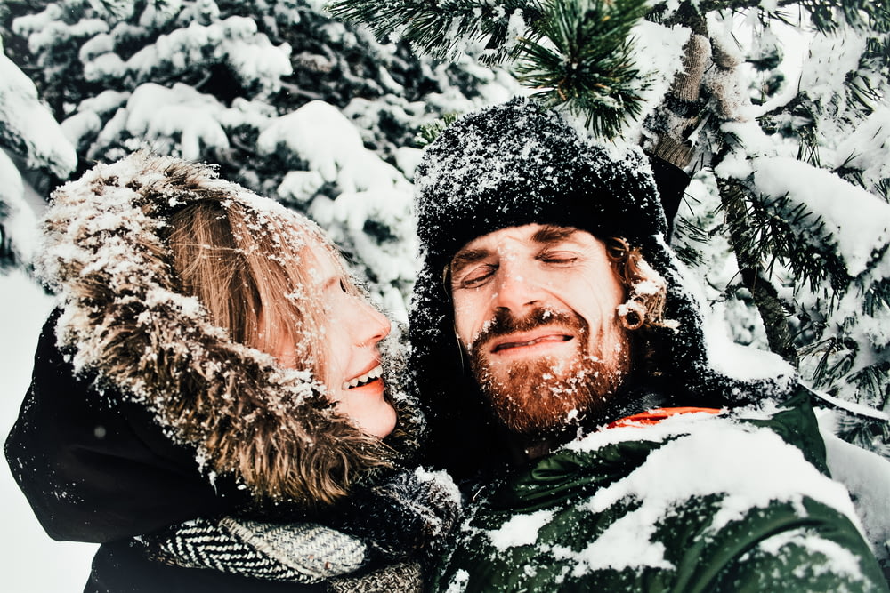 hombre y mujer sonrientes de pie bajo un árbol cubierto de nieve