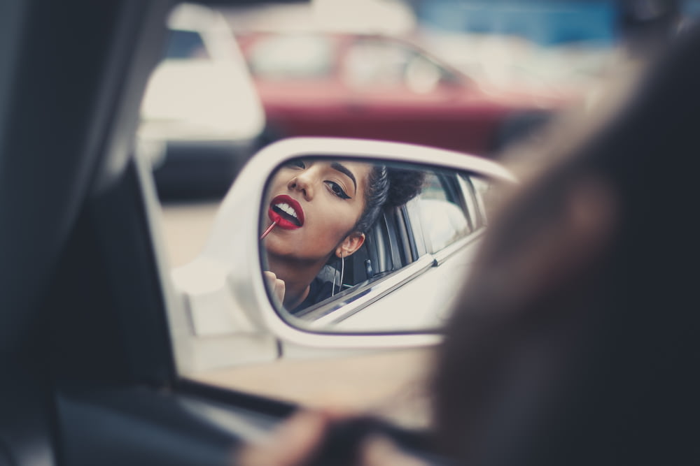 femme mettant du rouge à lèvres liquide sur ses lèvres tout en regardant le rétroviseur du véhicule pendant la journée