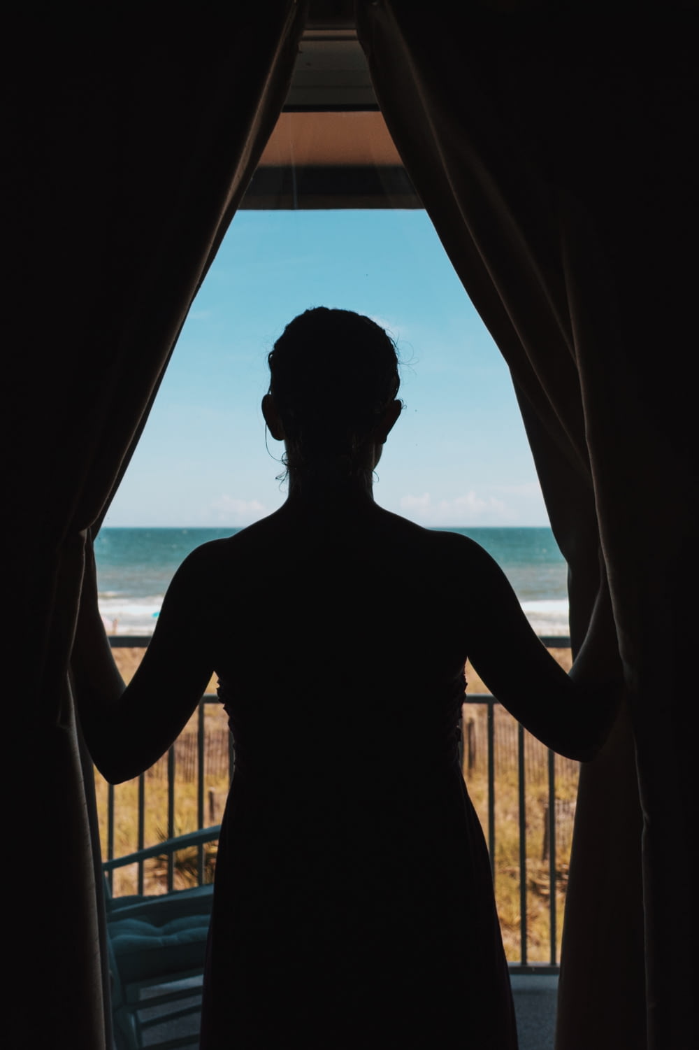 silhouette photo of woman standing between curtains